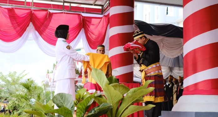 📷 Petugas pembawa Baki sedang menerima Bendera dari Inspektur Upacara di atas panggung kehormatan. (Humas Setda).
